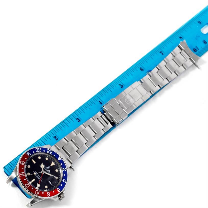 The image shows a top-down view of a Rolex Vintage Collection 16750 Men's Stainless Steel Black Dial 16750 Men's Stainless Steel Black Dial watch with a bezel and metal bracelet next to a blue ruler.