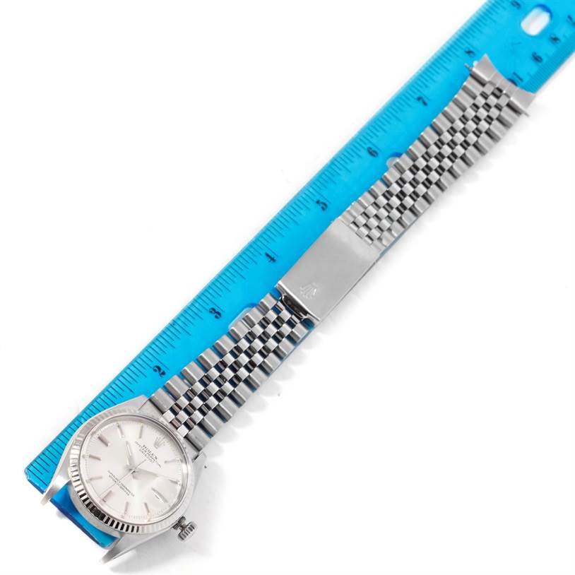 The Rolex Vintage Collection 1601 Men's Stainless Steel Silver Dial 1601 Men's Stainless Steel Silver Dial watch is shown from above, displaying its face, crown, and metal bracelet next to a blue ruler.