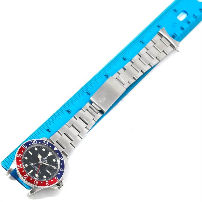 The image shows a top-down view of a Rolex Vintage Collection 1675 Men's Stainless Steel Black Dial 1675 Men's Stainless Steel Black Dial watch with a blue and red bezel, alongside a blue ruler.