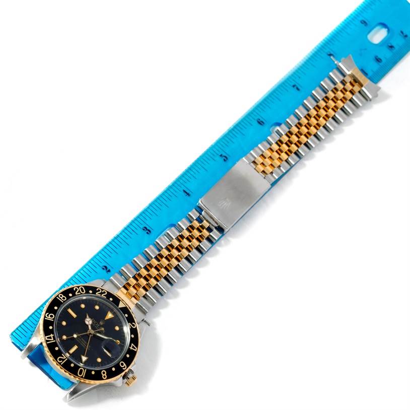 The Vintage Collection model by Rolex is shown flat, highlighting its gold and silver band and black dial, with a ruler for scale.