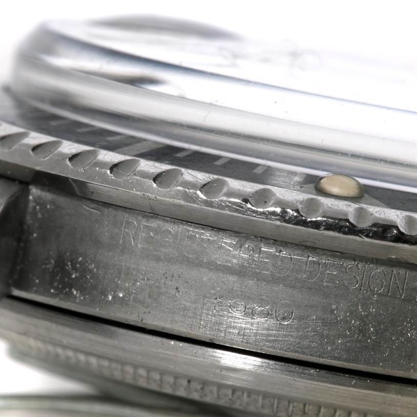 A close-up of the side view of a Rolex Vintage Collection 1680 Men's Stainless Steel Black Dial 1680 Men's Stainless Steel Black Dial watch, showing the bezel, crystal, and part of the case with engraved text.