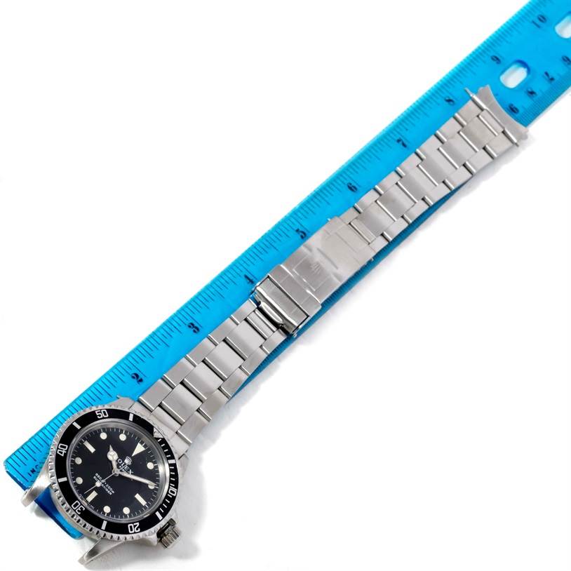 The image shows a Rolex Vintage Collection 5513 Men's Stainless Steel Black Dial 5513 Men's Stainless Steel Black Dial watch with a stainless steel bracelet laid beside a blue ruler for measurement.