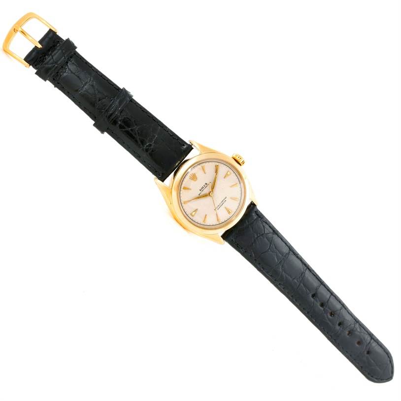 The image shows a full, top-down view of a Rolex Vintage Collection 6084 Men's Yellow Gold Silver Dial 6084 Men's Yellow Gold Silver Dial watch with a gold case and black leather strap.