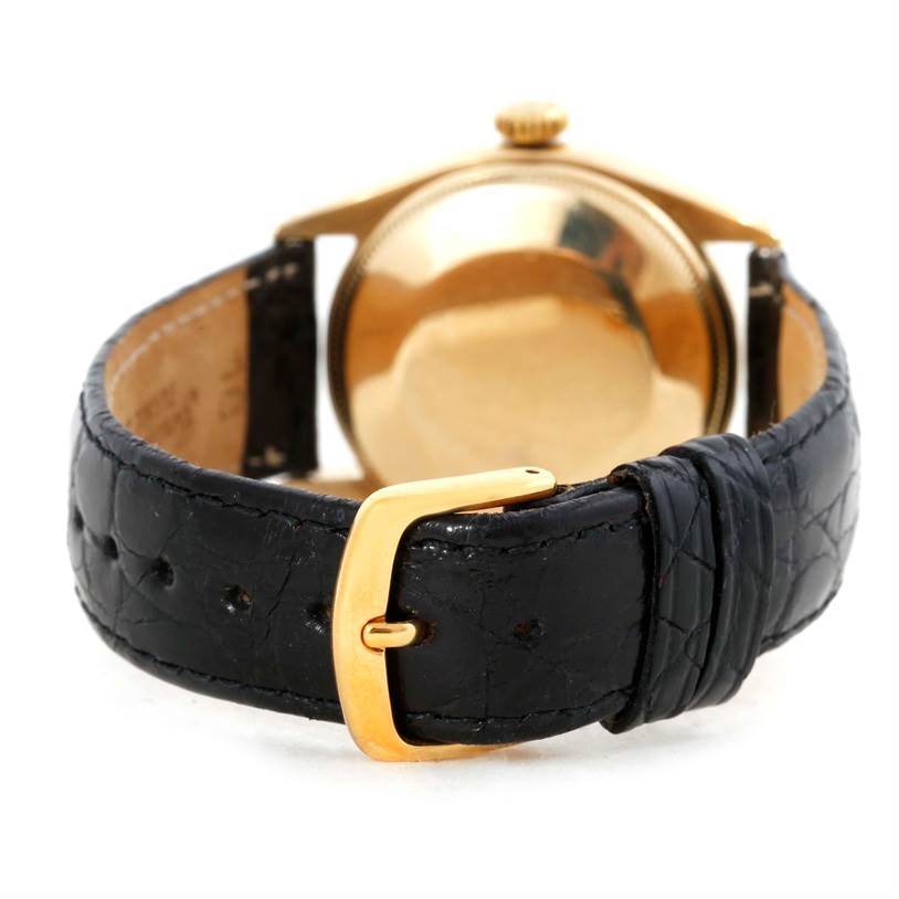 The image shows the back view of a Rolex Vintage Collection 6084 Men's Yellow Gold Silver Dial 6084 Men's Yellow Gold Silver Dial watch featuring a gold case and black leather strap with a gold buckle.