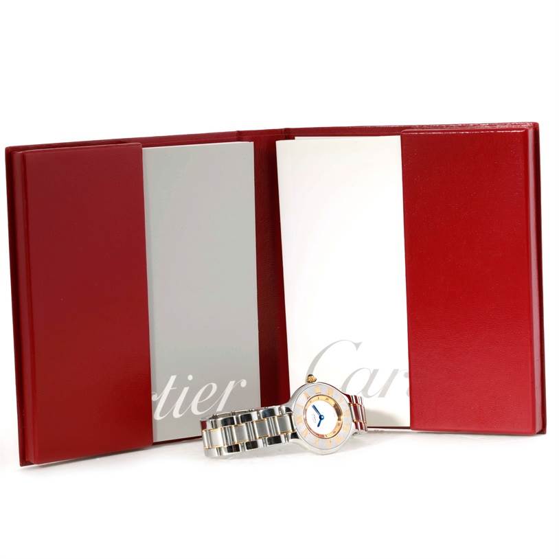 The image shows a Cartier Must 21 W10073R6 Women
s Stainless Steel Silver Dial W10073R6 Women
s Stainless Steel Silver Dial model watch with its booklet, displayed at an angle showing the face and bracelet.