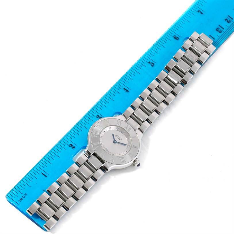 The Cartier Must 21 W10109T2 Women's Stainless Steel Silver Dial W10109T2 Women's Stainless Steel Silver Dial watch is shown horizontally, with its entire bracelet and face visible, placed against a blue ruler.