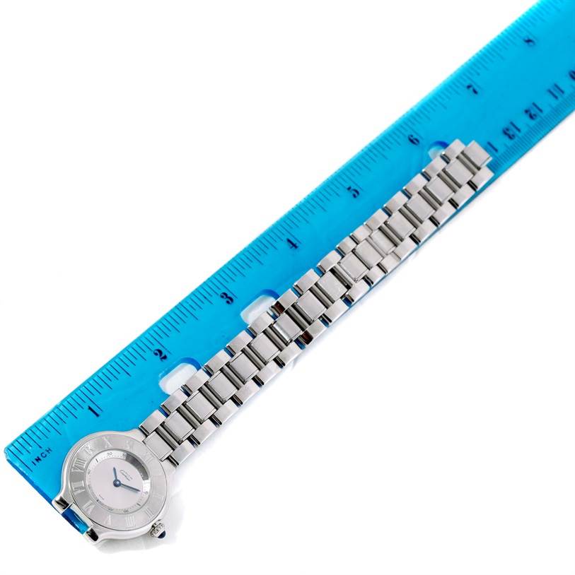 The image shows a Cartier Must 21 W10109T2 Men
s Stainless Steel Silver Dial W10109T2 Men
s Stainless Steel Silver Dial watch laid flat next to a ruler, displaying the watch
s face and metal bracelet.