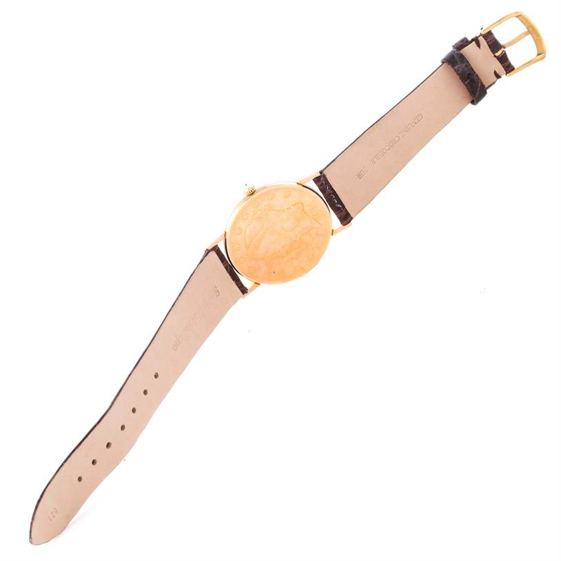 The image shows the Corum Coin Watch Men's Yellow Gold Black Dial Men's Yellow Gold Black Dial model from a flat, top-down angle, displaying the strap, case back, and clasp.