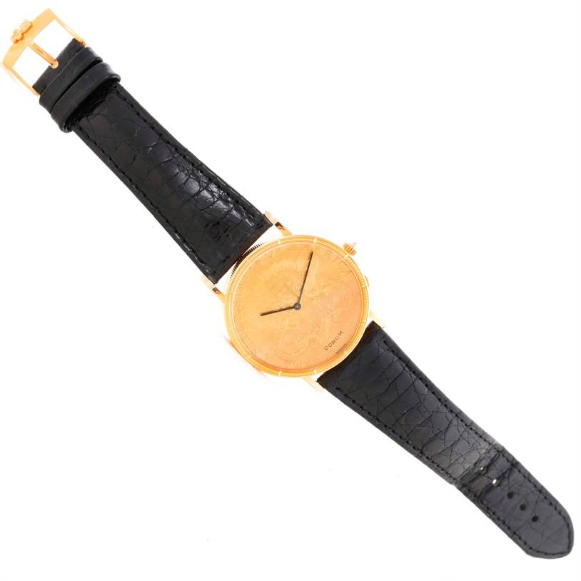 The Coin Watch model by Corum is shown at a top-down angle, displaying its black leather strap and gold coin-like face.