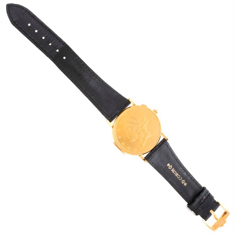The image shows a Corum Coin Watch Men's Yellow Gold Black Dial Men's Yellow Gold Black Dial model, displayed flat with a gold case and black leather strap, viewed from above.