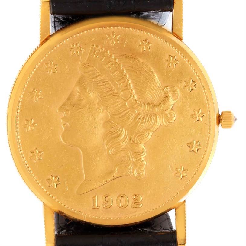 The image shows a front view of the Coin Watch model by Corum, featuring a black leather strap and a gold coin dial with "1902" engravings.