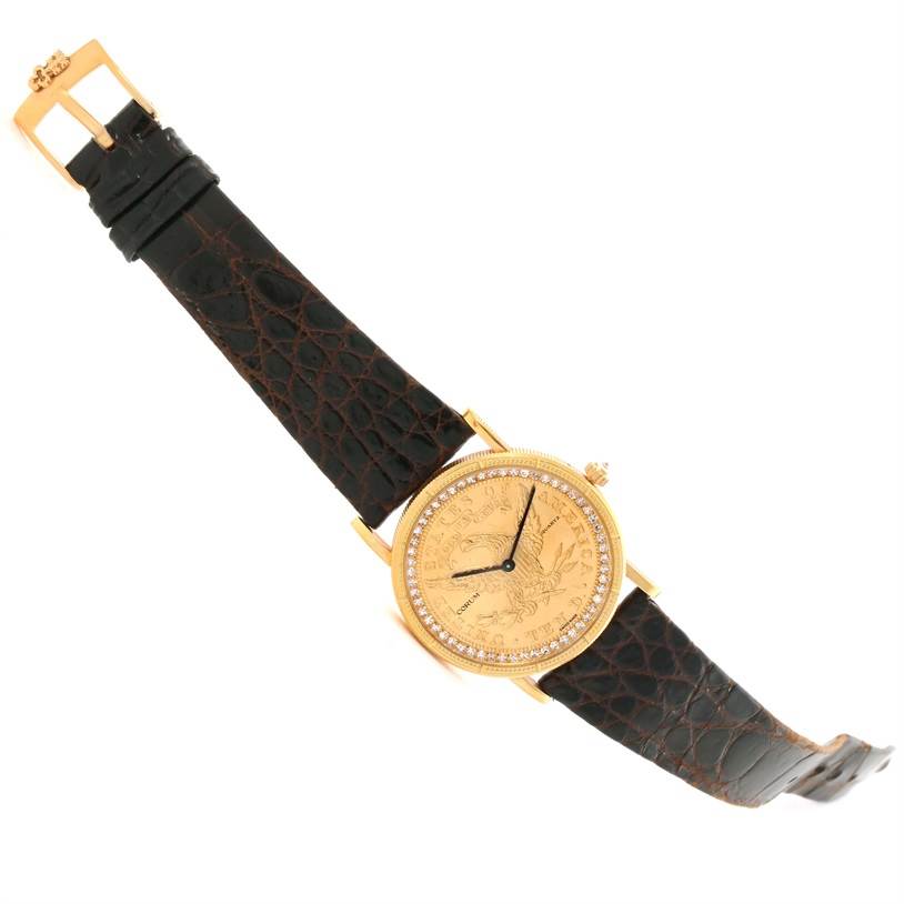 The Corum Yellow Gold Black Dial Yellow Gold Black Dial 1893 18K Yellow Gold 10 Coin Diamond Watch is shown at an angled view, highlighting its gold case, diamond bezel, and black leather strap.