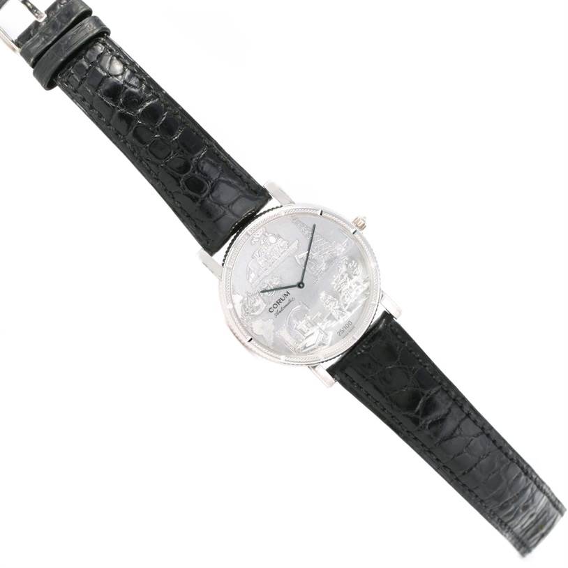 The image shows a Corum Men's White Gold White Dial Men's White Gold White Dial Celebrates Second Millennium 18K White Gold Automatic LTD Watch from a top-down angle, highlighting its face and leather strap.