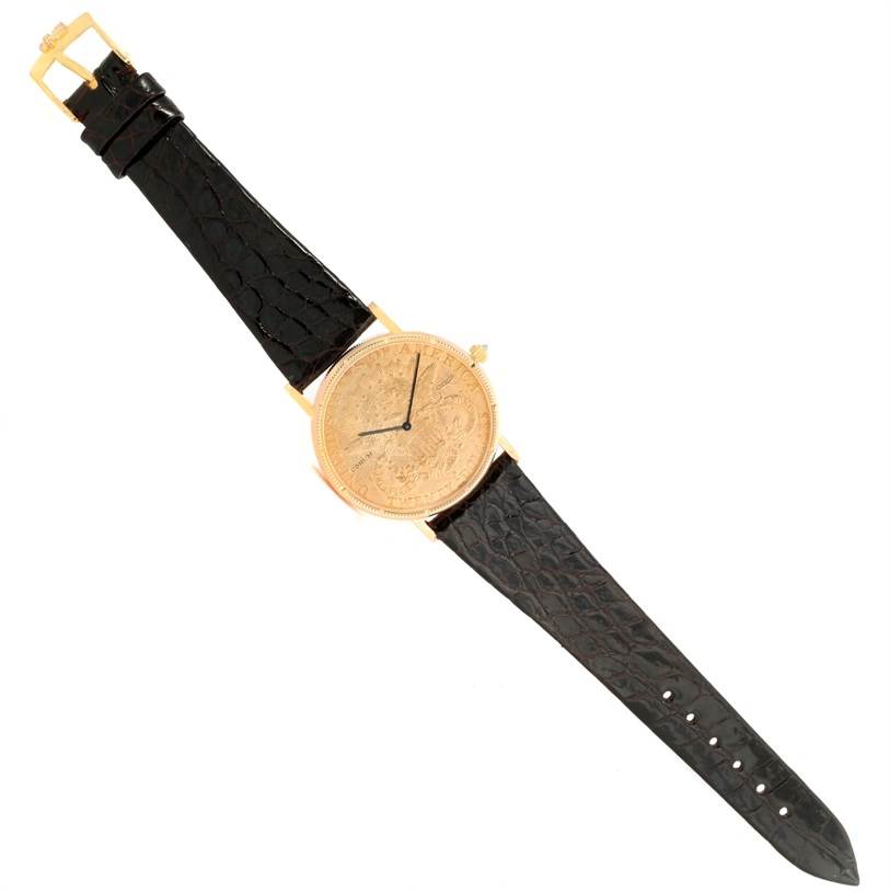 The Corum Coin Watch Men's Yellow Gold Black Dial Men's Yellow Gold Black Dial model is shown from a top-down angle, displaying its entire face, bezel, and black leather strap.