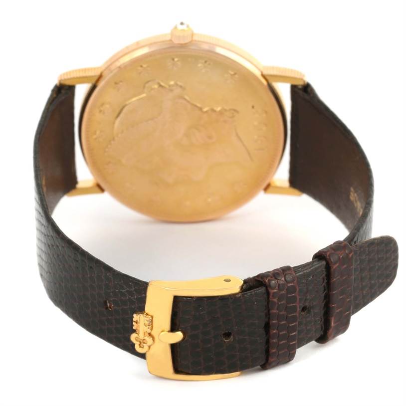 The image shows the back of the Coin Watch by Corum, focusing on the leather strap and gold buckle.