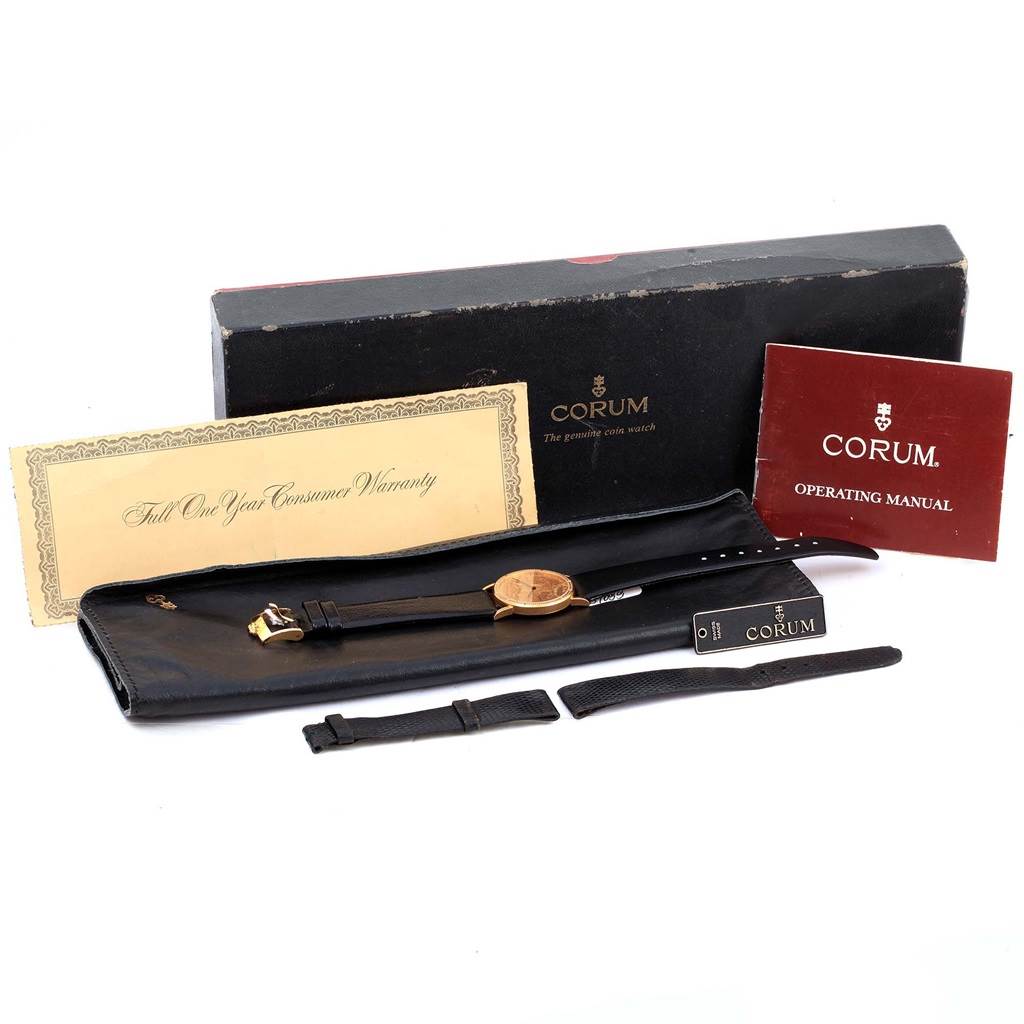 The image shows an open box with the Corum Women's Yellow Gold Black Dial Women's Yellow Gold Black Dial 18K Yellow Gold 10 Dollars Coin Ladies Watch, warranty card, straps, and the operating manual.