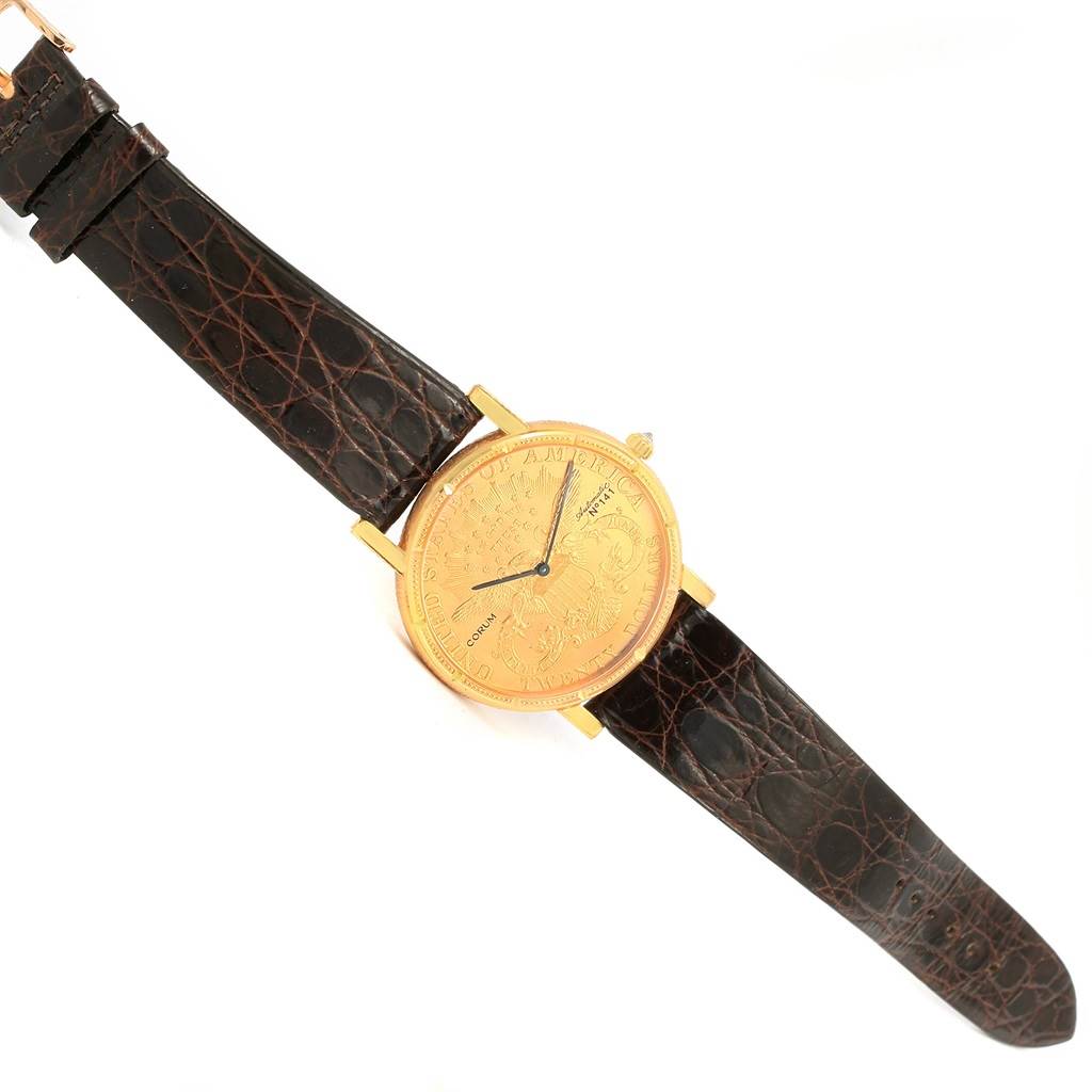 The image shows a Corum Coin Watch Men's Yellow Gold Black Dial Men's Yellow Gold Black Dial displayed flat from an overhead angle, highlighting its gold face and brown leather strap.