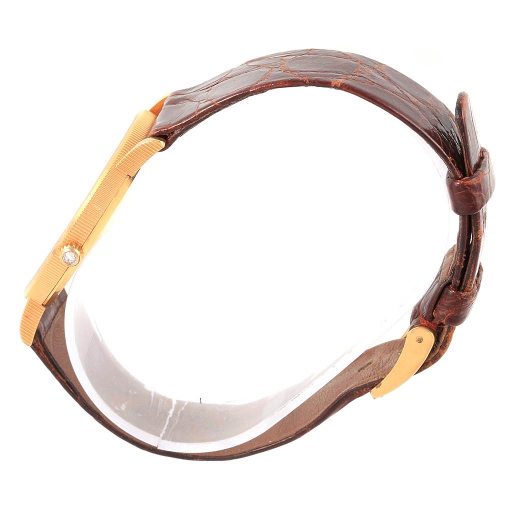 The image shows a side view of the Corum Coin Watch Men's Yellow Gold Black Dial Men's Yellow Gold Black Dial model, focusing on the gold case, diamond crown, and brown leather strap.