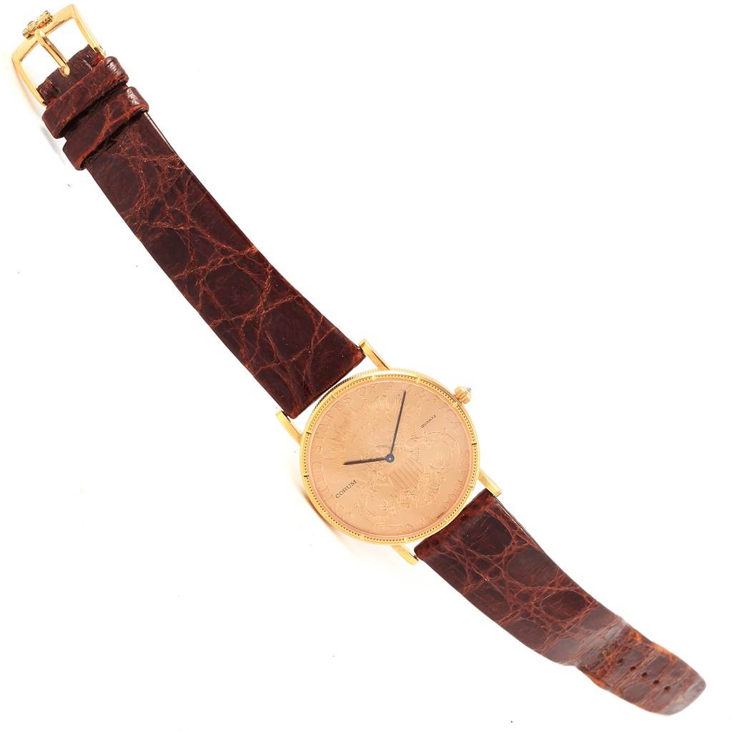 The image shows a Corum Coin Watch Men's Yellow Gold Black Dial Men's Yellow Gold Black Dial model laid flat, highlighting its dial, leather strap, and buckle from a top-down angle.