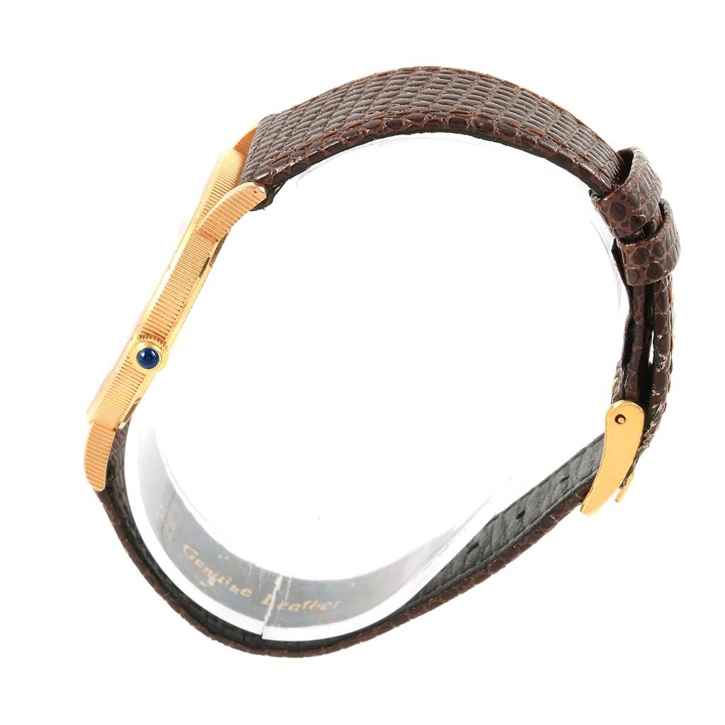 This image shows a side view of the Corum Coin Watch Men's Yellow Gold Black Dial Men's Yellow Gold Black Dial, highlighting its textured strap and gold-tone case with a blue cabochon crown.