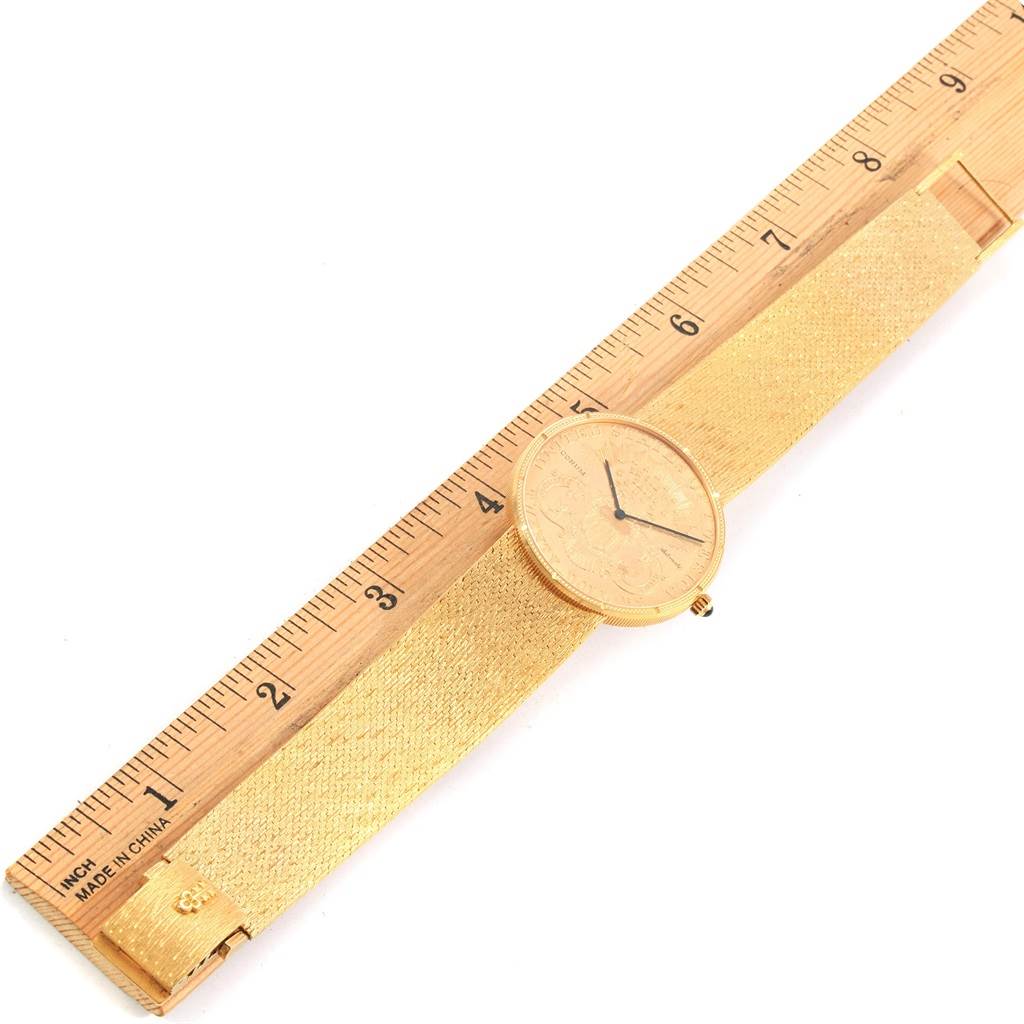 The image shows a Corum Coin Watch Men's Yellow Gold Black Dial Men's Yellow Gold Black Dial placed alongside a measuring ruler, highlighting its face and gold mesh strap.
