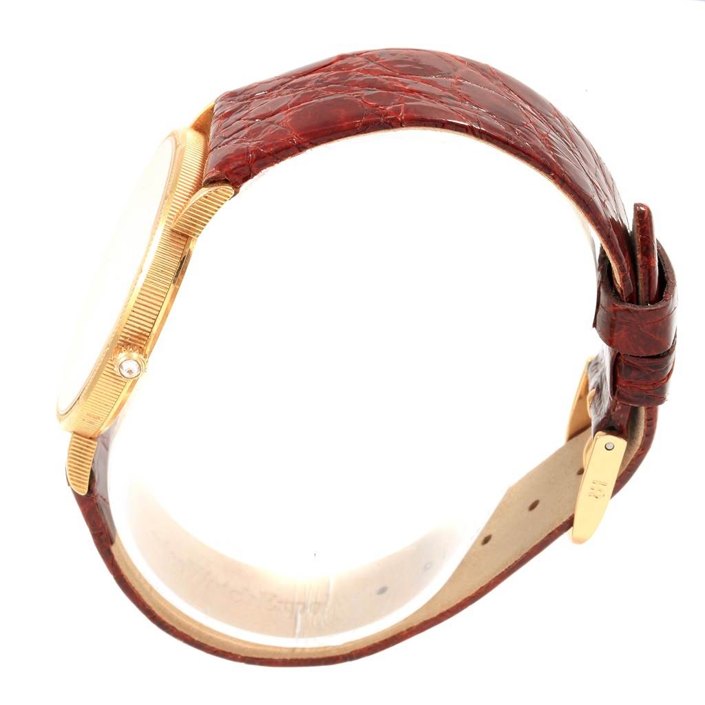 The image shows a side view of a Corum Coin Watch Men's Yellow Gold Black Dial Men's Yellow Gold Black Dial model, displaying its gold case, crown, and brown leather strap.