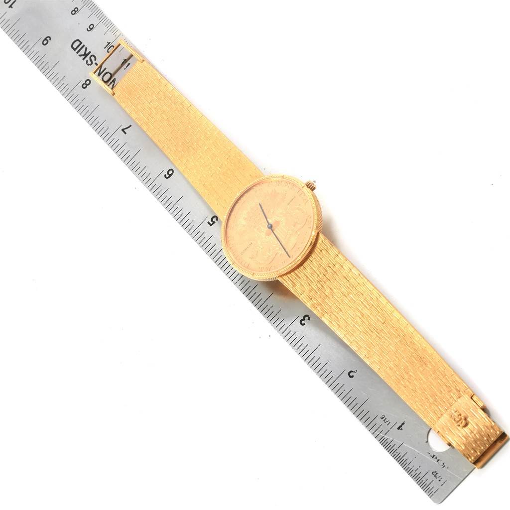 The image shows a Corum Coin Watch Men's Yellow Gold Black Dial Men's Yellow Gold Black Dial model laid flat alongside a ruler, displaying the watch face and golden strap.