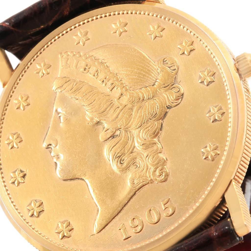 The image shows a close-up view of the face of a Corum Coin Watch  Men's Yellow Gold Black Dial  Men's Yellow Gold Black Dial model, featuring a gold coin design with the year 1905, crown, and parts of its strap.