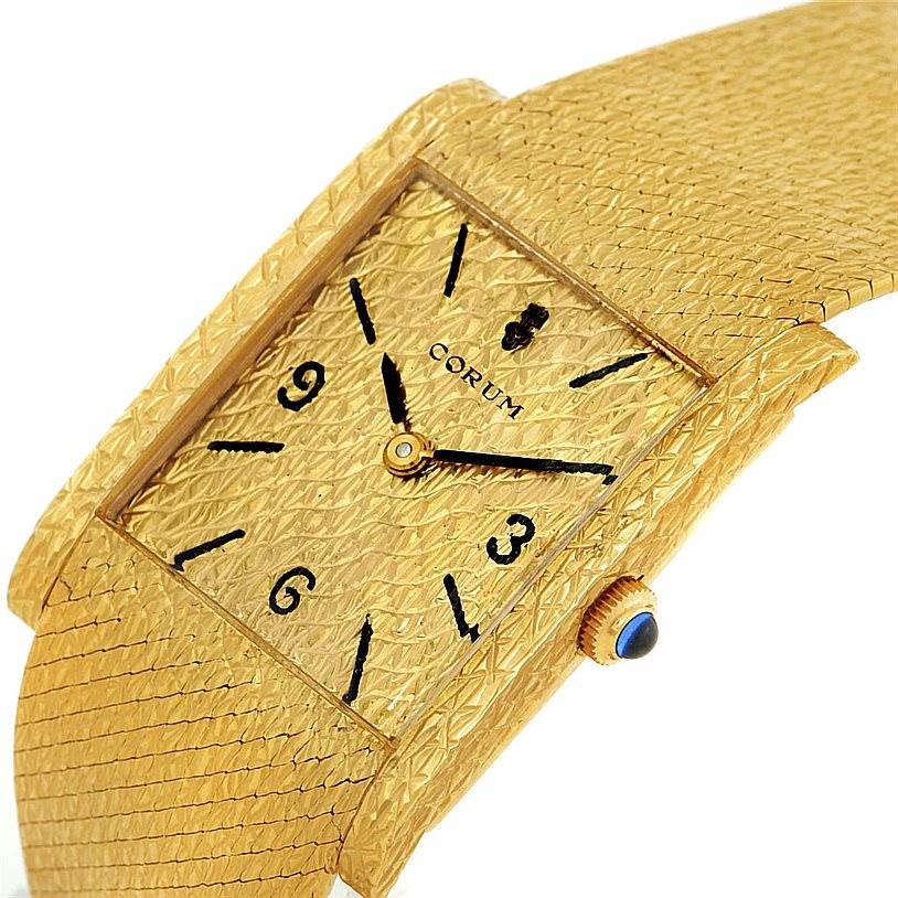 The image shows an angled view of a Vintage Corum watch, highlighting its textured gold face, black numerals, and gold crown with blue detail.