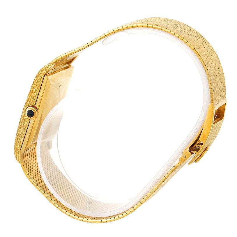 The image shows a side view of a vintage Corum watch, highlighting its gold band, intricate clasp, and case with a crown adorned with a blue gem.