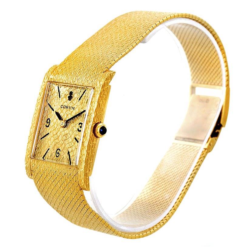 The image shows a side angle of a rectangular gold textured watch by Corum Vintage 8764 Men's Yellow Gold Champagne Dial 8764 Men's Yellow Gold Champagne Dial, displaying its face, strap, and crown.