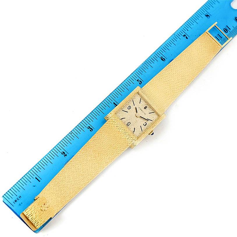 The image shows a top-down view of a vintage Corum watch, including its face, case, band, and a ruler for scale.