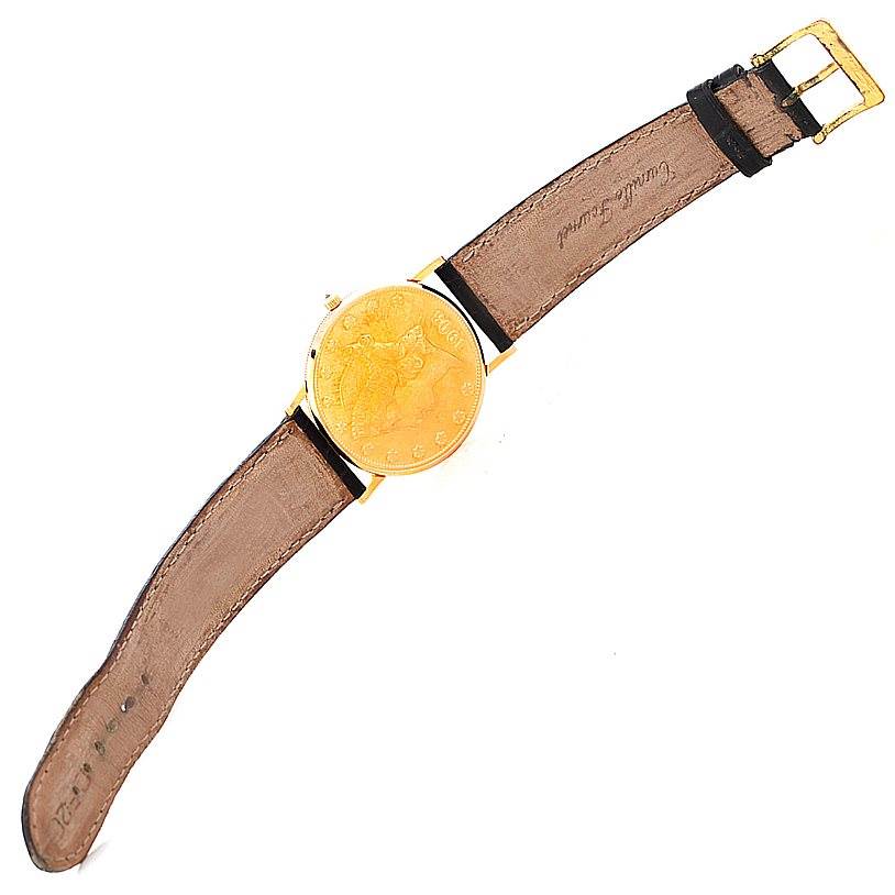 The image shows a top-down view of a Corum Coin Watch Men's Yellow Gold Black Dial Men's Yellow Gold Black Dial model, displaying its watch face, leather strap, and buckle.
