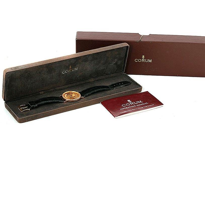 The image displays a Corum Coin Watch Men's Yellow Gold Black Dial Men's Yellow Gold Black Dial in its case along with its packaging box and manual from a top-down angle.