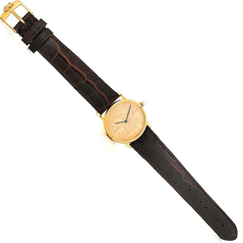 The image shows a top view of a Corum Women's Yellow Gold Black Dial Women's Yellow Gold Black Dial Ladies 18K Yellow Gold 10 Dollars Coin Watch, highlighting the entire watch and brown strap.