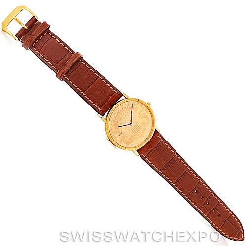 This image shows the Corum Coin Watch Men's Yellow Gold Black Dial Men's Yellow Gold Black Dial model laid flat, displaying its round golden face and brown leather strap from a top-down angle.