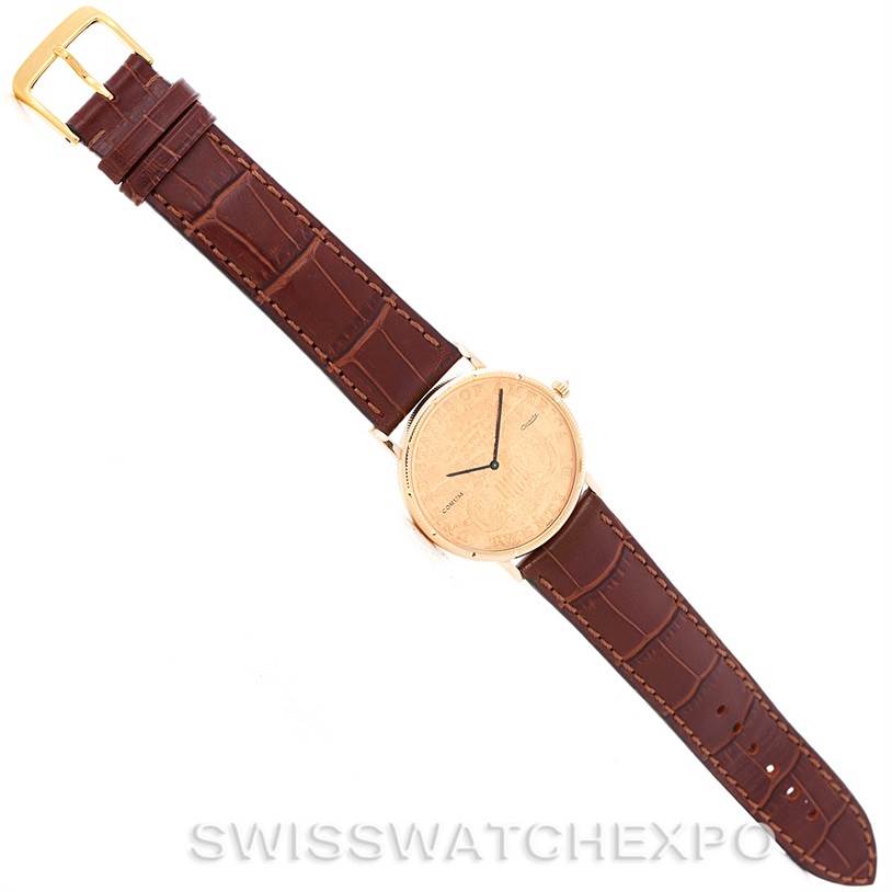 The Corum Coin Watch Men's Yellow Gold Black Dial Men's Yellow Gold Black Dial model is shown from a top-down angle, displaying its face, leather strap, and buckle.