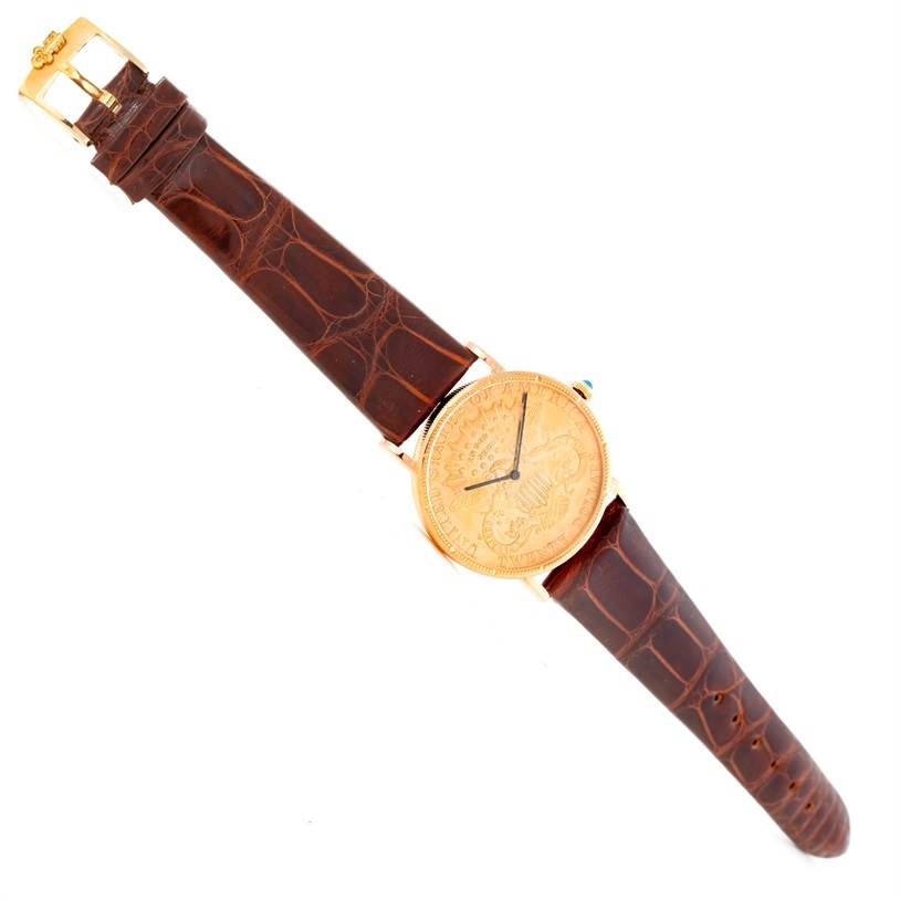 The image shows a top view of a Corum Coin Watch Men's Yellow Gold Black Dial Men's Yellow Gold Black Dial model, displaying the watch face, brown leather strap, and gold buckle.