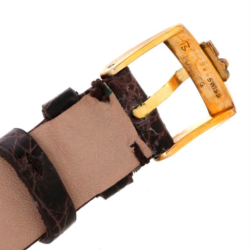 The image shows the gold buckle and part of the leather strap for the Corum Women's Yellow Gold Black Dial Women's Yellow Gold Black Dial 22K Yellow Gold 10 Dollars Coin Diamond Ladies Watch model.