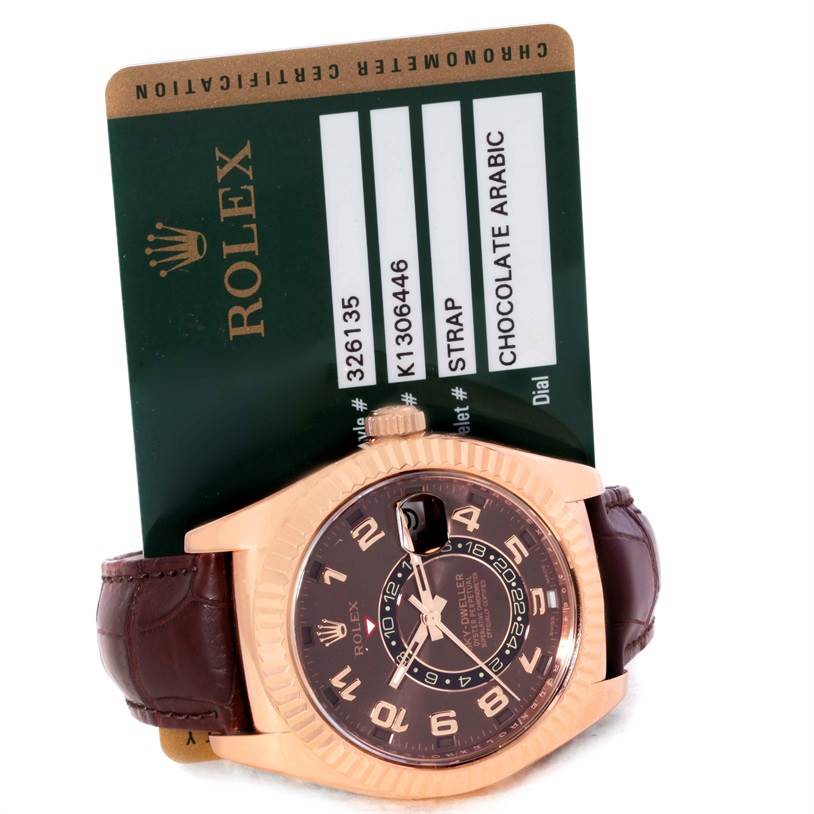 The image shows a front angled view of a Rolex Sky-Dweller 326135 Men
s Rose Gold Brown Dial 326135 Men
s Rose Gold Brown Dial watch with a chocolate Arabic dial and leather strap, alongside its certification card.