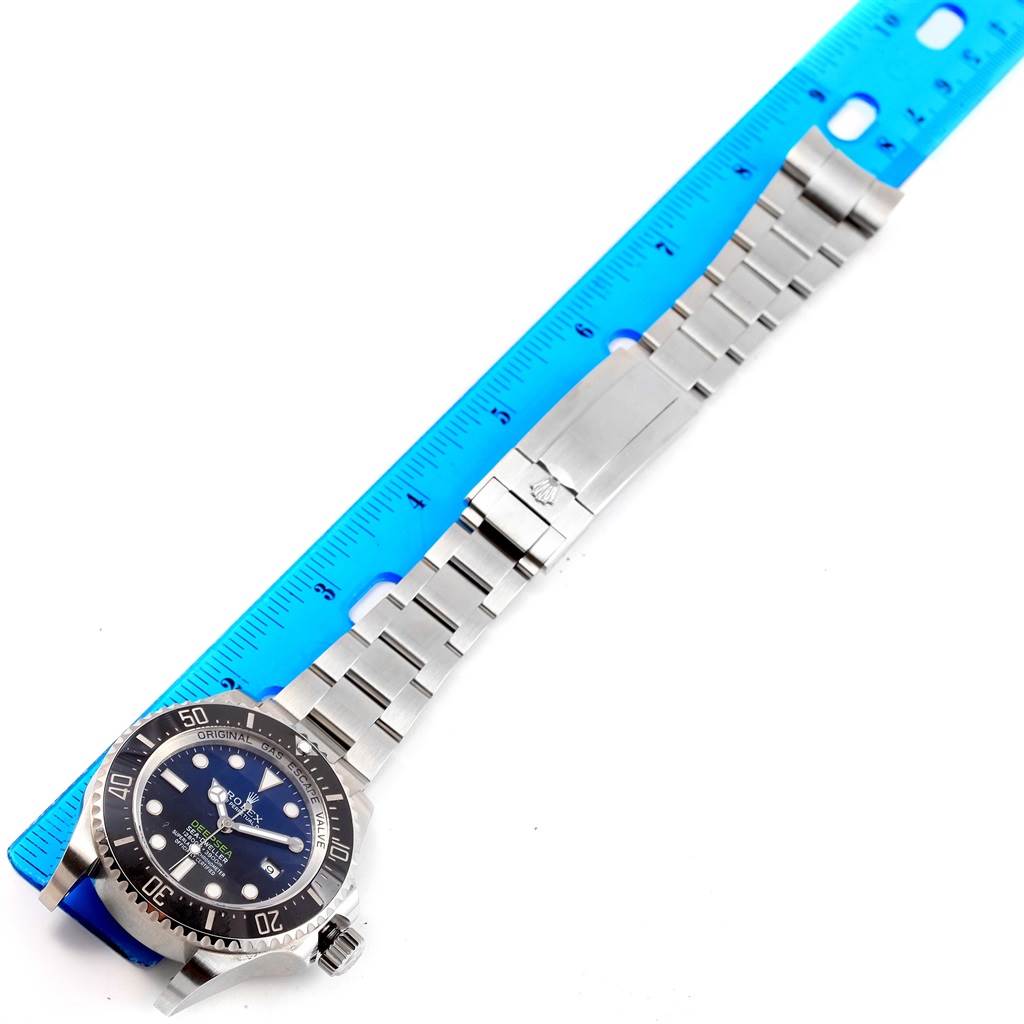 The image shows a top view of a Rolex Sea-Dweller 116660 Men's Stainless Steel Blue Dial 116660 Men's Stainless Steel Blue Dial watch, including its face, bezel, crown, and metal bracelet, alongside a blue ruler.