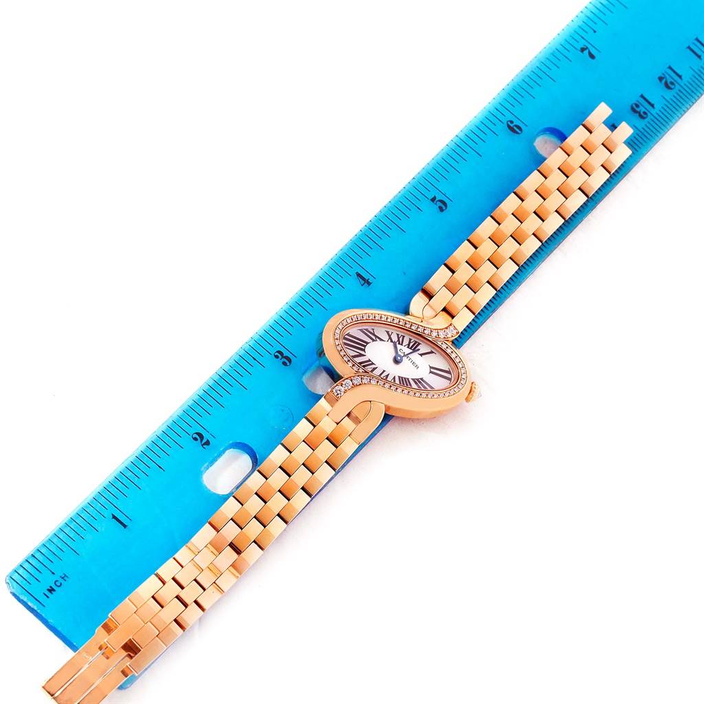 The Delices model by Cartier is shown from a top-down angle next to a blue ruler, highlighting its face and band.