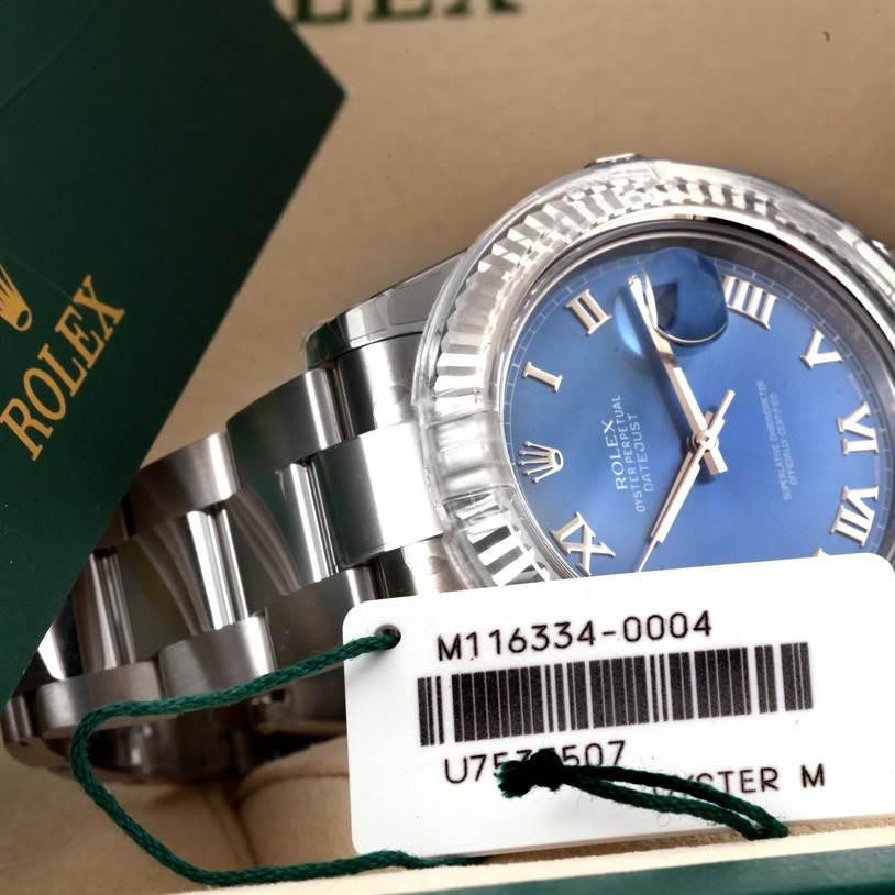 The image shows a close-up of a Rolex Datejust 41 116334BLRO Men's Stainless Steel Blue Dial 116334BLRO Men's Stainless Steel Blue Dial watch with a blue dial and part of the bracelet, along with a tag and packaging.