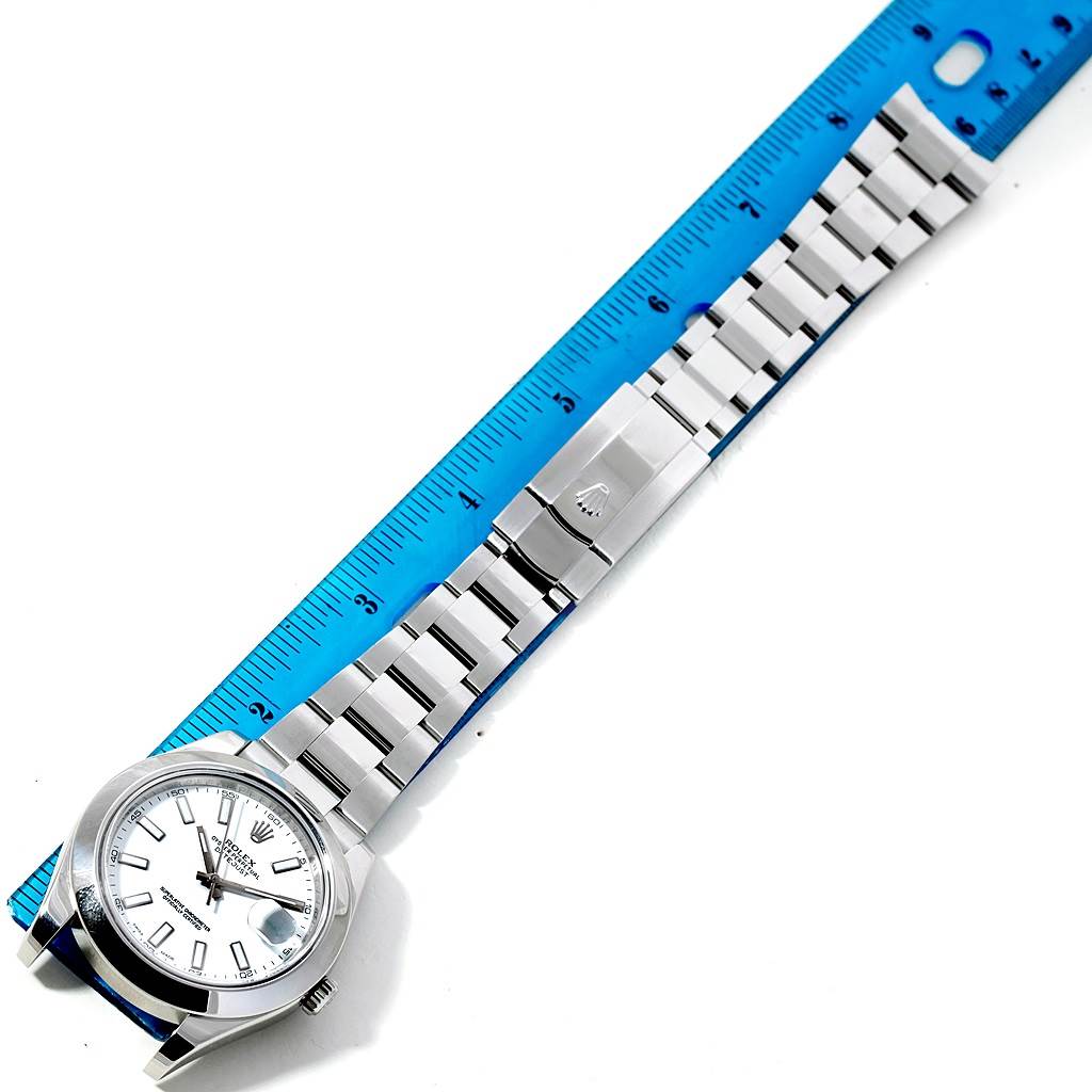 The image shows a top-down view of a Rolex Datejust 41 116300 Men's Stainless Steel White Dial 116300 Men's Stainless Steel White Dial watch, displaying its face, bezel, and metal bracelet against a blue ruler.