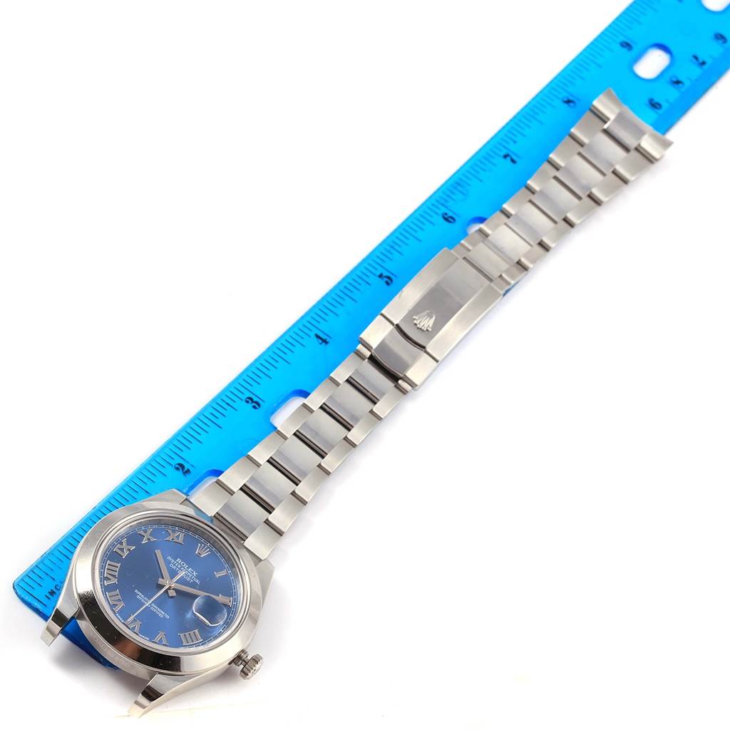 The Rolex Datejust 41 116300 Men
s Stainless Steel Blue Dial 116300 Men
s Stainless Steel Blue Dial watch is displayed flat, showing its blue dial, case, bracelet, and clasp alongside a blue ruler.