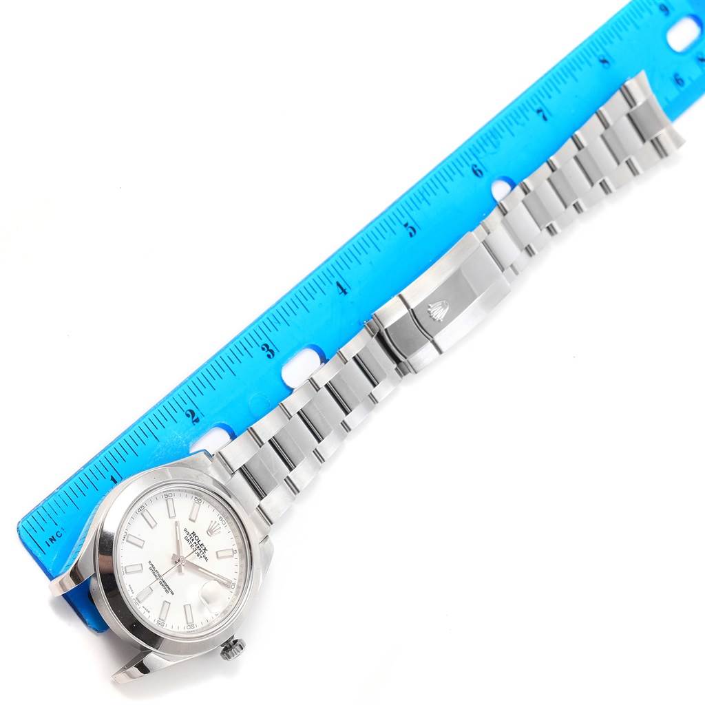 The Rolex Datejust 41 116300 Men
s Stainless Steel White Dial 116300 Men
s Stainless Steel White Dial watch is shown horizontally with its face, bracelet, and clasp next to a blue ruler.