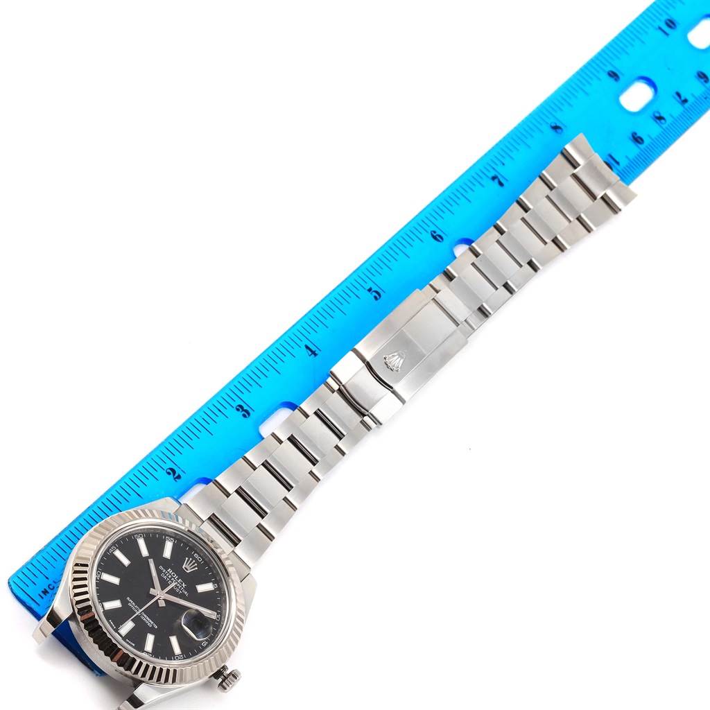 The Rolex Datejust 41 116334 Men's Stainless Steel Black Dial 116334 Men's Stainless Steel Black Dial watch is shown laid flat, highlighting the face, bracelet, and clasp beside a blue ruler.