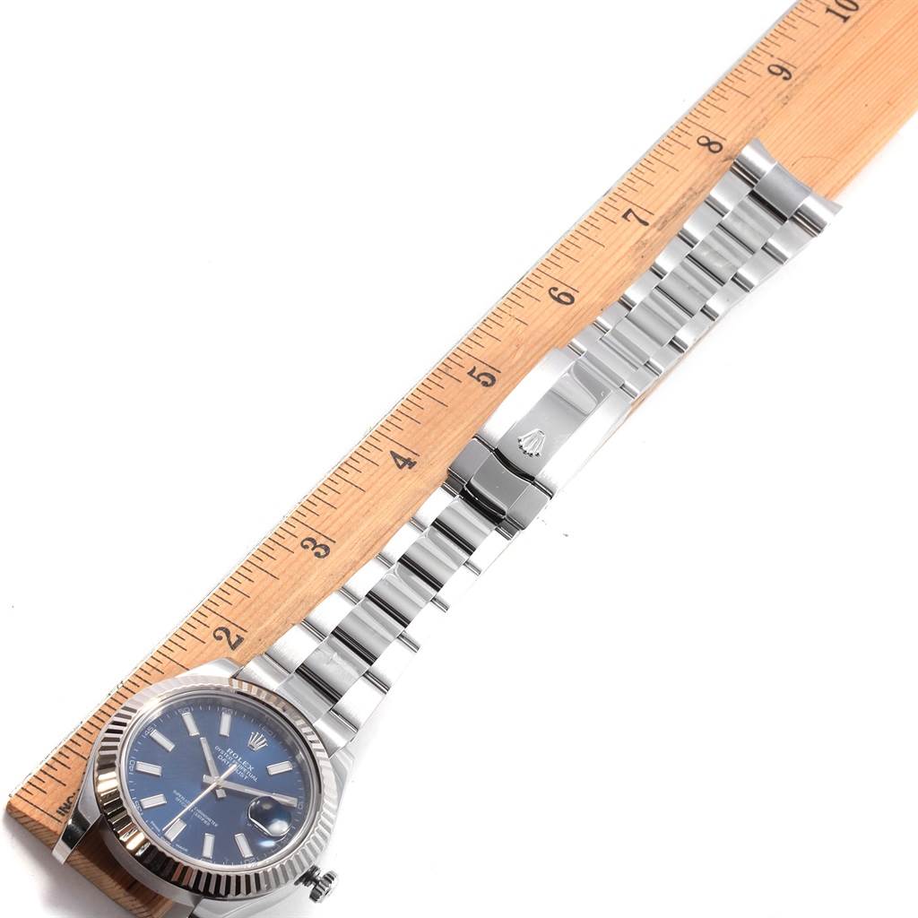 The image shows a Rolex Datejust 41 116334 Men's Stainless Steel Blue Dial 116334 Men's Stainless Steel Blue Dial watch laid flat, displaying its blue dial, fluted bezel, and metal bracelet alongside a ruler.
