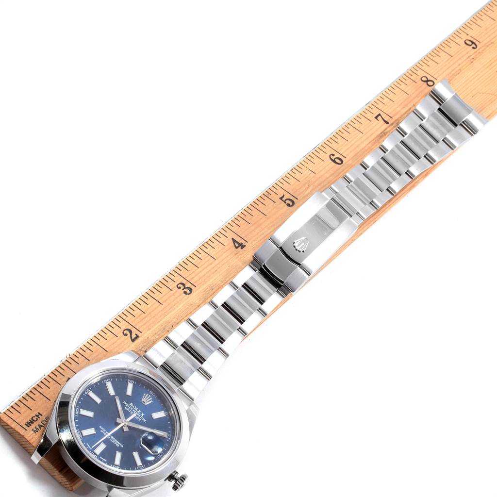 This image shows a top-down view of the Rolex Datejust 41 116300 Men's Stainless Steel Blue Dial 116300 Men's Stainless Steel Blue Dial watch with its bracelet laid out next to a ruler.