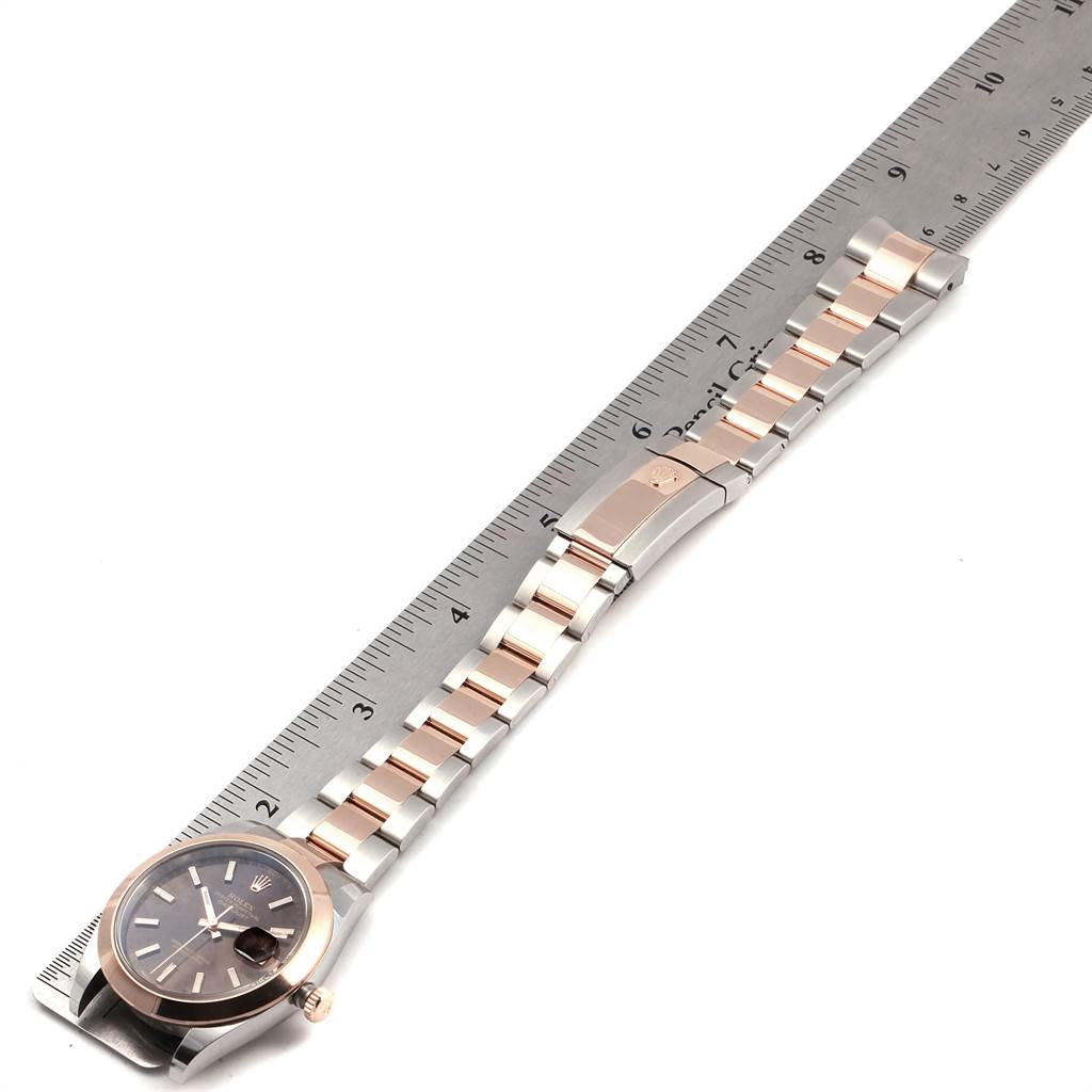 The photo shows a side angle of the Rolex Datejust 41 126301 Men
s Steel and Gold (two tone) Brown Dial 126301 Men
s Steel and Gold (two tone) Brown Dial watch, highlighting its face, bracelet, and clasp alongside a ruler for measurement.